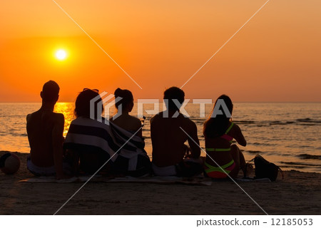 Silhouettes a young people sitting on a beach looking at sunset Silhouettes a young people sitting on a beach looking at sunset 12185053