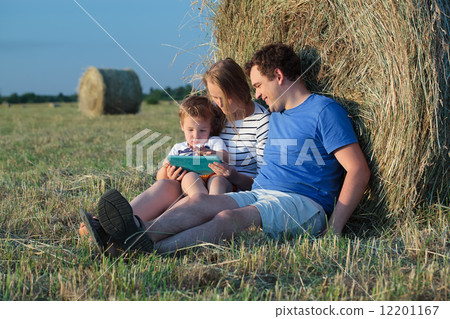 Family of three with pad in the field with hay rolls 12201167