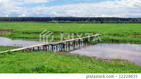 Wooden bridge over river in green field near forest Wooden bridge over river in green field near forest 12228635