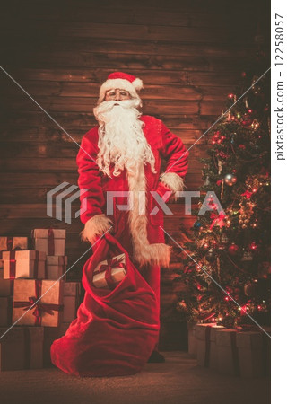 Santa Claus in wooden home interior with sack full of Christmas presents Santa Claus in wooden home interior with sack full of Christmas presents 12258057