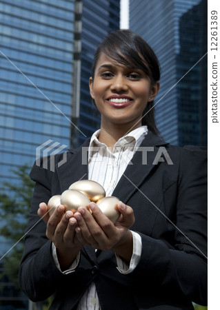 Businesswoman holding gold eggs outdoors Businesswoman holding gold eggs outdoors 12261389