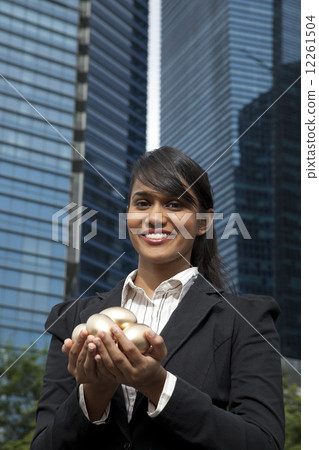 Businesswoman holding gold eggs outdoors 12261504