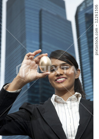 Businesswoman holding up gold egg outdoors Businesswoman holding up gold egg outdoors 12261506