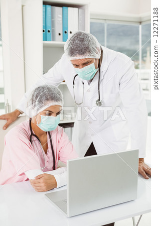 Doctors wearing surgical masks while using laptop at medical office Doctors wearing surgical masks while using laptop at medical office 12271188