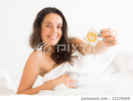 Smiling woman holding condom in bed 12276089