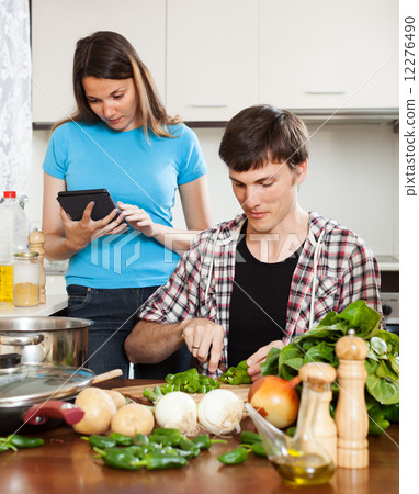 Man cooking food while woman reading eBook Man cooking food while woman reading eBook 12276490