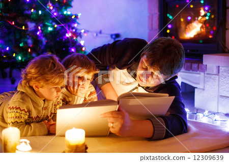 Young father and his little sons reading book by a fireplace on Young father and his little sons reading book by a fireplace on 12309639