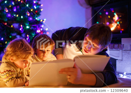 Young father and his little sons reading book by a fireplace on Young father and his little sons reading book by a fireplace on 12309640