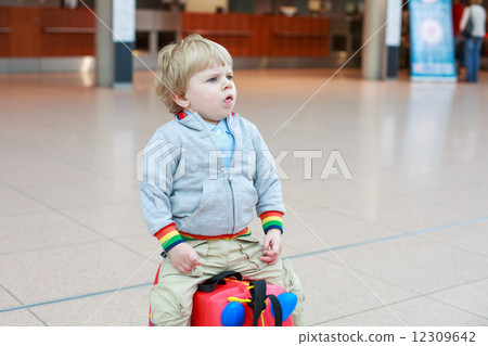 Funny toddler boy going on vacations trip with suitcase at airpo 12309642