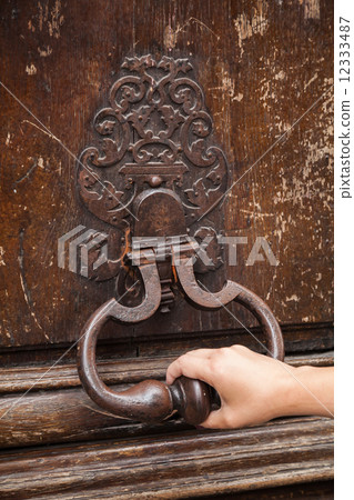 Hand and old rusted knocker on brown wooden door in Paris, Franc Hand and old rusted knocker on brown wooden door in Paris, Franc 12333487