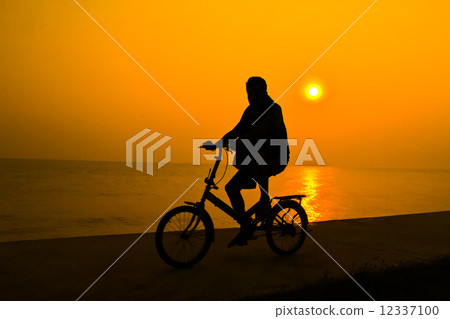 siluette of person who rides a bicycle near sea water with the s 12337100