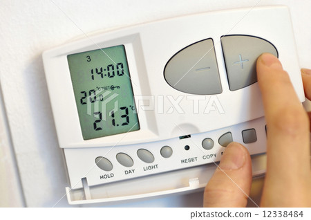hand pressing button on digital thermostat 12338484
