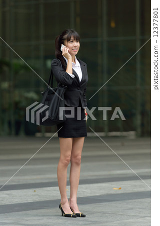One young successful chinese business woman with bag making mobile call outside office building 12377801