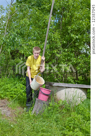 The boy, the teenager, pours water in a bucket from a well The boy, the teenager, pours water in a bucket from a well 12387045