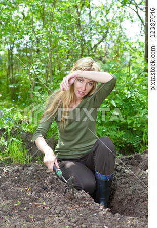 The young woman couch a garden-bed with the first sprouts on a summer cottage.. The young woman couch a garden-bed with the first sprouts on a summer cottage.. 12387046