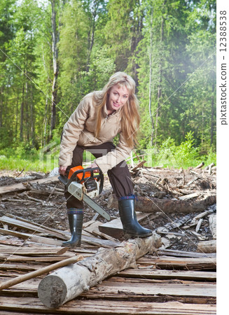 The young woman in wood saws a tree a chain saw The young woman in wood saws a tree a chain saw 12388538