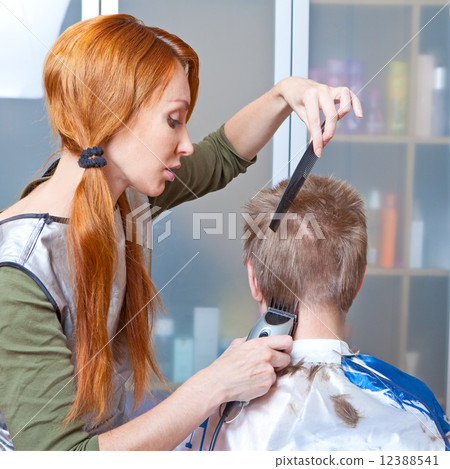 The beautiful young woman the hairdresser does a hairstyle to the client - young man The beautiful young woman the hairdresser does a hairstyle to the client - young man 12388541