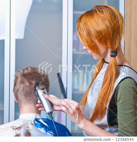 The beautiful young woman the hairdresser does a hairstyle to the client - young man The beautiful young woman the hairdresser does a hairstyle to the client - young man 12388543