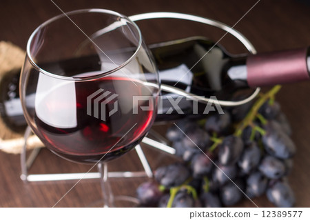 Wineglass with red wine with grapes and bottle at background 12389577