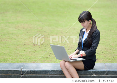 One young successful Chinese business woman sitting along promenade using laptop 12393748