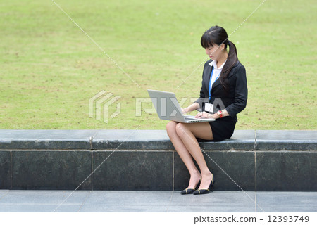 One young successful Chinese business woman sitting along promenade using laptop One young successful Chinese business woman sitting along promenade using laptop 12393749