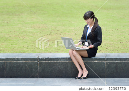 One young successful Chinese business woman sitting along promenade using laptop One young successful Chinese business woman sitting along promenade using laptop 12393750