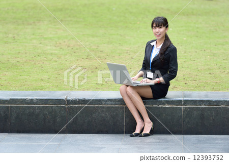 One young successful Chinese business woman sitting along promenade using laptop 12393752