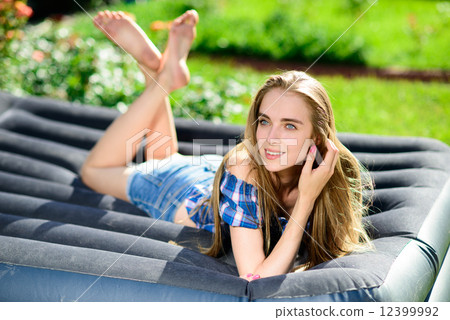 Happy young woman lying on the matrass in the garden 12399992