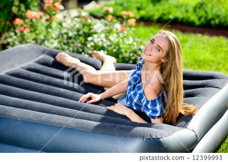Happy young woman lying on the matrass in the garden Happy young woman lying on the matrass in the garden 12399993