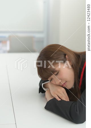 A businesswoman falls asleep with her head on her desk, exhausted. A businesswoman falls asleep with her head on her desk, exhausted. 12423480