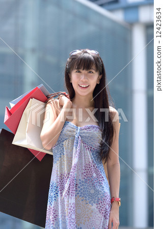Young chinese woman shopping with shopping bags standing outside of mall along promenade 12423634
