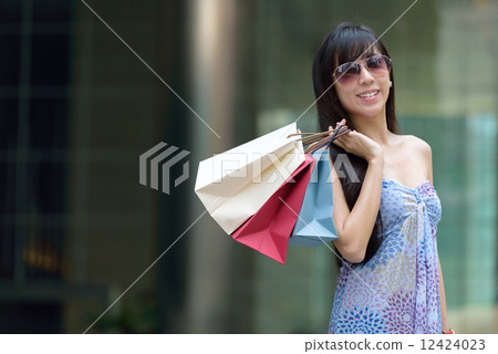 Young chinese woman shopping with sunglass shopping bags standing outside of mall along promenade 12424023
