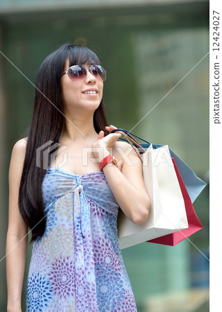 Young chinese woman shopping with sunglass shopping bags standing outside of mall along promenade 12424027