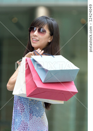 Young chinese woman shopping with sunglass shopping bags standing outside of mall along promenade 12424049