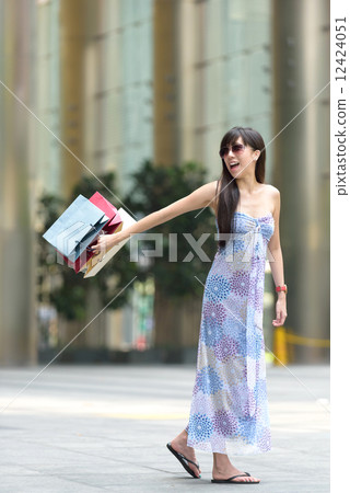 Young chinese woman shopping with sunglass shopping bags standing outside of mall along promenade 12424051