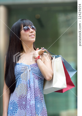 Young chinese woman shopping with sunglass shopping bags standing outside of mall along promenade 12424054
