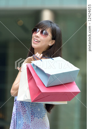 Young chinese woman shopping with sunglass shopping bags standing outside of mall along promenade 12424055