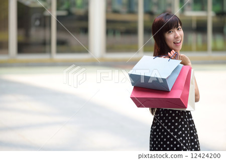 Young chinese woman shopping with shopping bags standing outside of mall along promenade 12424200