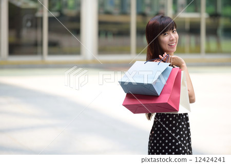 Young chinese woman shopping with shopping bags standing outside of mall along promenade 12424241