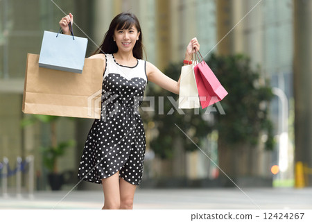 Young chinese woman shopping with shopping bags standing outside of mall along promenade 12424267