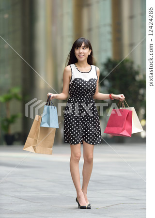Young chinese woman shopping with shopping bags standing outside of mall along promenade 12424286