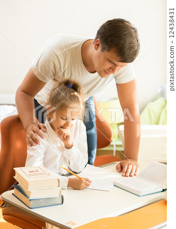 young father looking at daughter doing homework 12438431