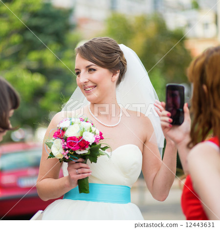 Bridesmaid is taking photo of a young happy bride 12443631