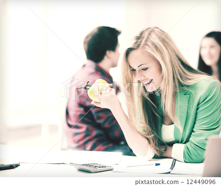 smiling student girl eating apple at school 12449096