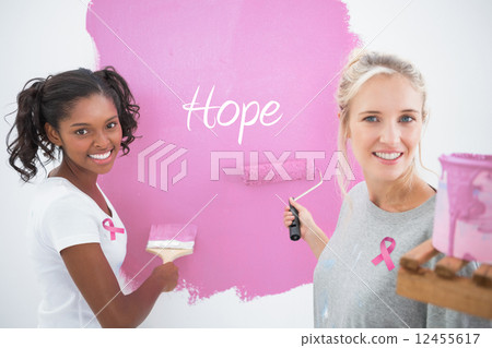 Composite image of smiling housemates painting wall pink 12455617