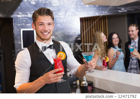 Handsome barman smiling at camera holding cocktails 12471792
