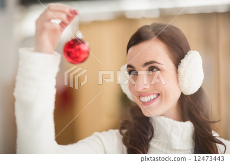 Pretty brunette with ear muffs holding bauble Pretty brunette with ear muffs holding bauble 12473443