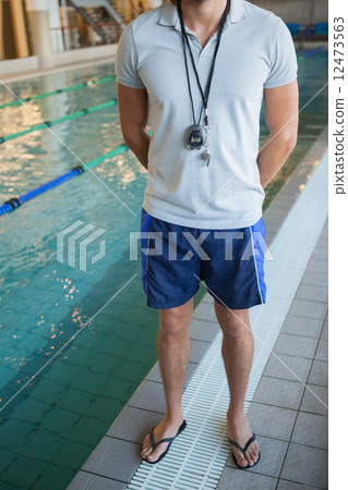 Low section of a swimming coach with stopwatch by pool 12473563