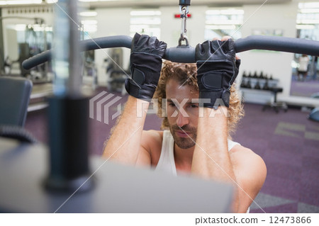 Young man exercising on a lat machine in gym Young man exercising on a lat machine in gym 12473866