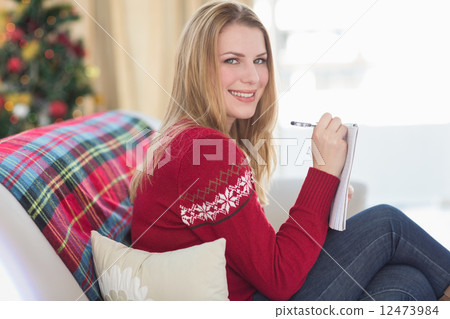Smiling blonde writing while sitting on the sofa Smiling blonde writing while sitting on the sofa 12473984